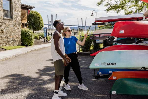 Two people stand next to a group of kayaking, getting ready to choose one and go out on the Hudson River.