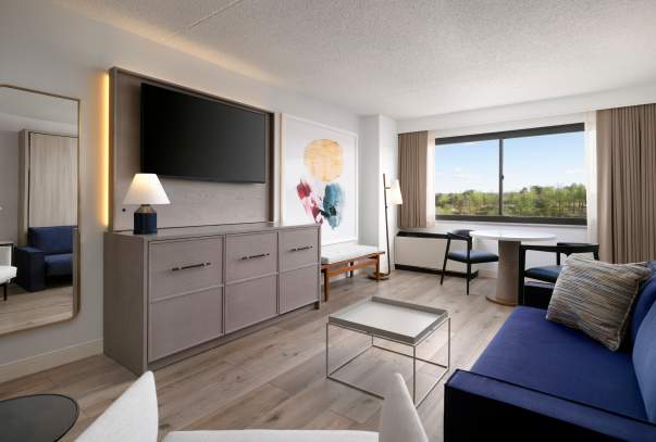 The seating area of a hotel room with a blue couch and grey furniture.