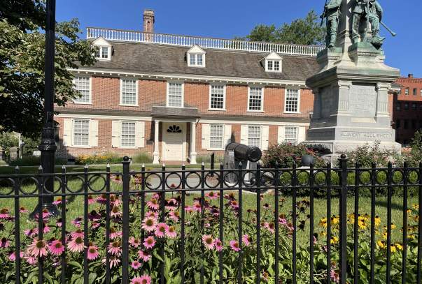 The exterior of Philipse Manor Hall with purple and yellow flowers blooming in the foreground.