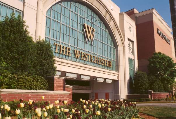 The outside of the building with light stone and glass plus a sign that says "The Westchester."