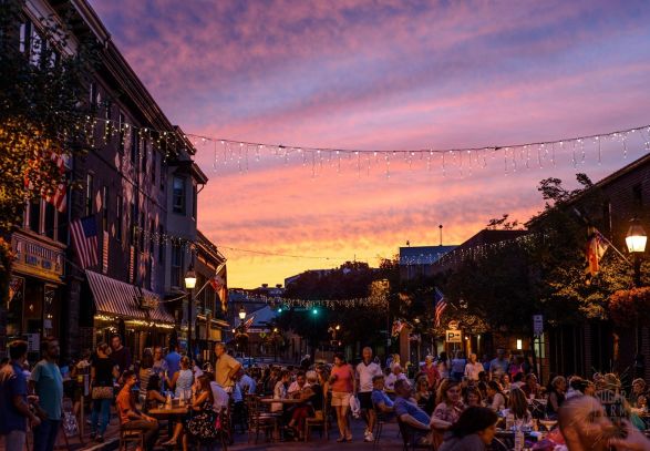 A street with dining tables and people,twinkle lights hung up during a sunset in Annapolis
