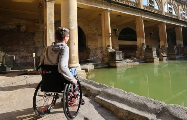 A man in a wheelchair looking at the Great Bath at The Roman Baths