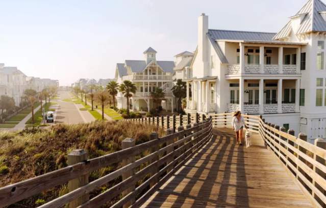 Women walking down a board walk with a white house in the back