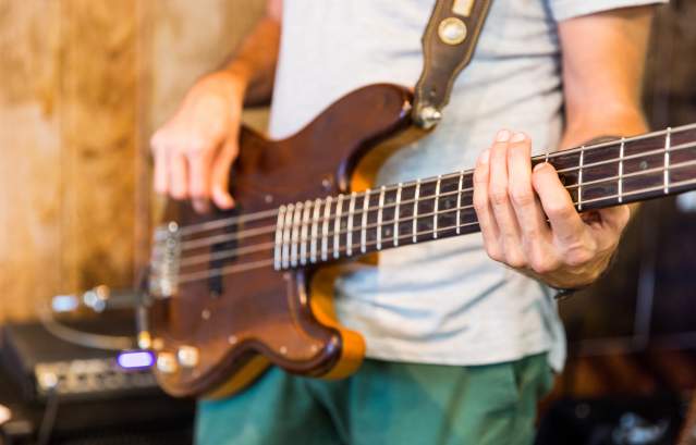 A close up of a guy strumming a brown guitar.