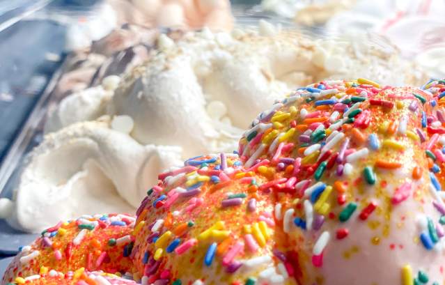 Up close shot of two gelato trays. One is pink and covered in sprinkles, the other white and covered in almonds.