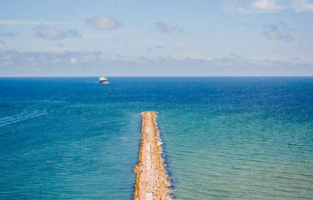 Rock jetty sticking out into the blue and green ocean on a sunny day.