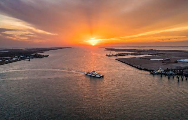 Ferry boat crossing over from one side to the other. Sun setting with orange and yellow colors spreading through the sky.