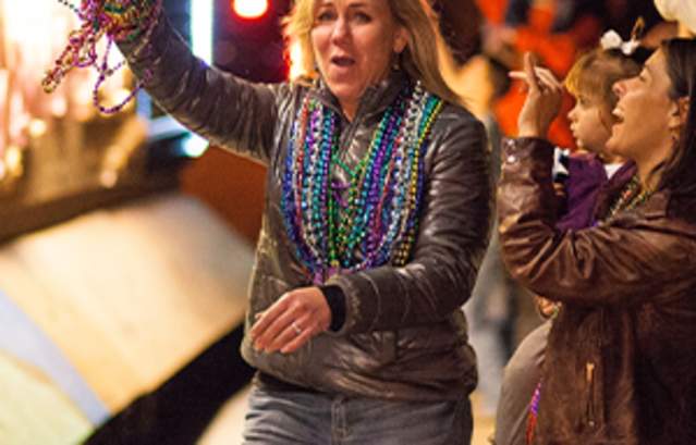 Woman celebrating at a Mardi Gras parade in a crowd, holding Mardi Gras beads