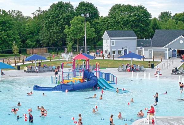 wide shot of kids in a pool with a small slide structure in the middle.