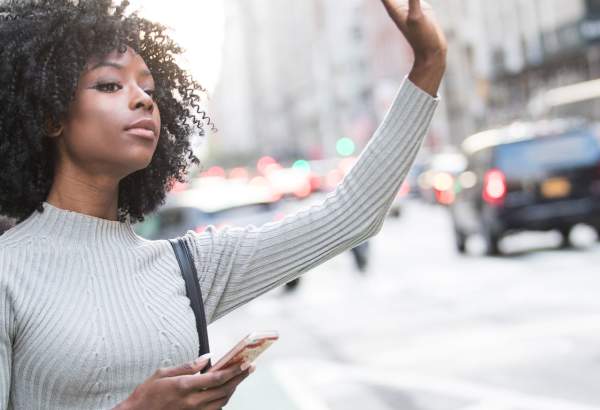 getting here woman signaling for a car while holding her phone