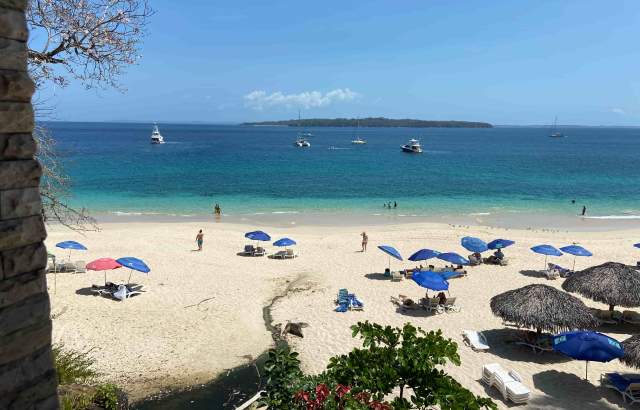 Tourists sunbathe. Blue umbrellas scattered on the beach, Boats on the water. Sunny day.