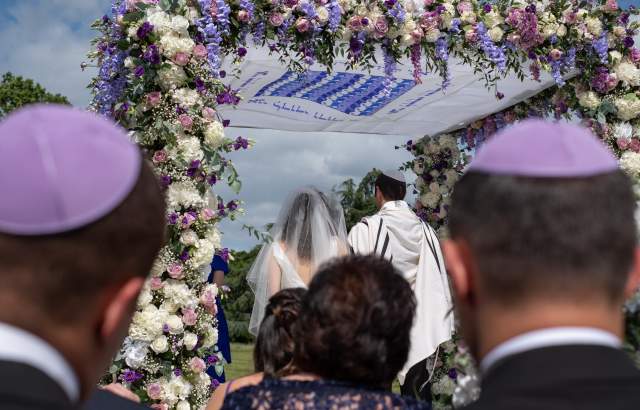 Jewish couple in a wedding ceremony under a floral chuppah wedding canopy.