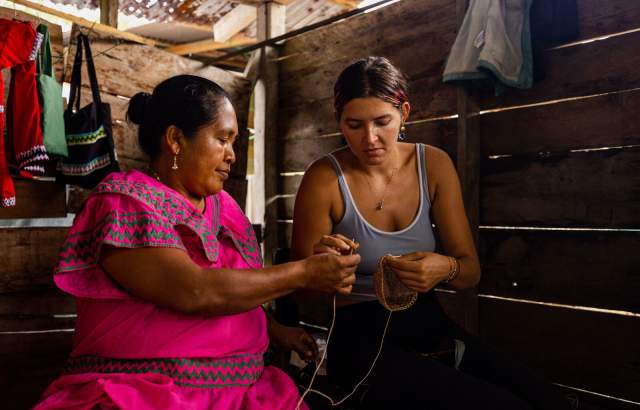 Ngäbe woman wearing  Nagua (traditional dress) hows visitor the weaving of a craft.