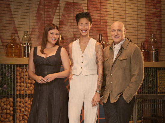 Top Chef Judges, Gail Simmons, Kristen Kish and Tom Colicchio standing on set in the Top Chef kitchen