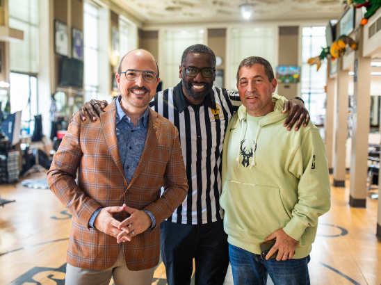 Three men standing together with arms around each other's shoulders at Gee's, smiling at the camera.