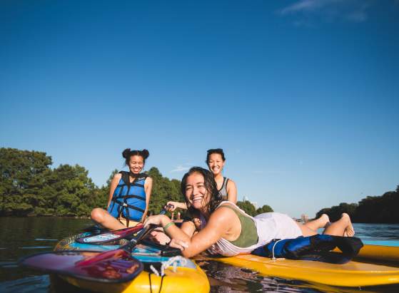 Photo of three women sitting on Lady Bird Lake paddle board rentals from Rowing Dock. They are looking and smiling at the camera, which sits at water-level