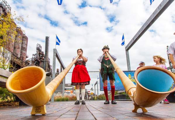 A man and woman in traditional German attire playing large trumpets on a stage