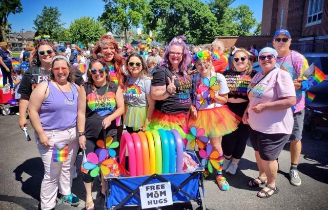 Group of people in colorful outfits with a rainbow wagon at the parade