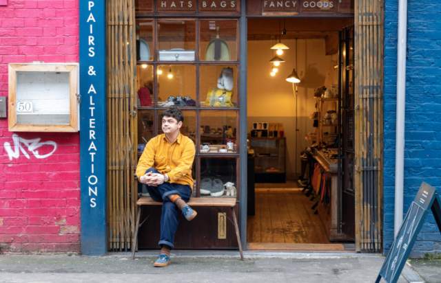 Liam, a shop owner based in Manchester, sat outside of his colourful shop.