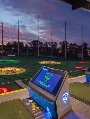 Golf bays at Topgolf Woodbury with sun setting in the background