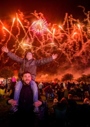 A father with child on shoulders with Fireworks display in sky