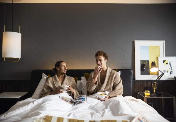 2 people in a hotel bed eating breakfast