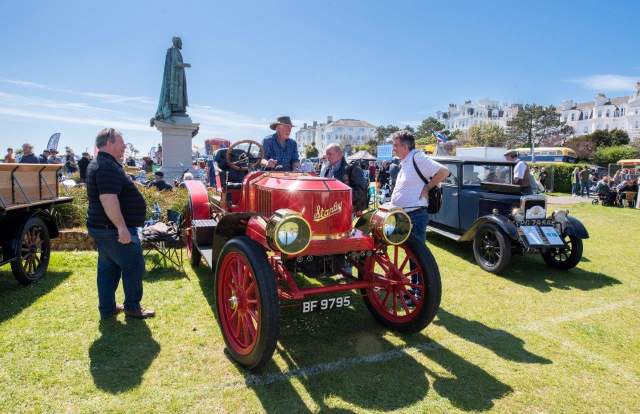 A group of men stand round a red vintage car parked on the green next to a statue in the seaside town of Eastbourne in Sussex