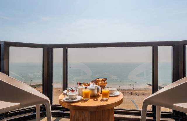 a balcony room at The View hotel in Eastbourne. There is a breakfast on the table, two chairs and a view over the sea and beach