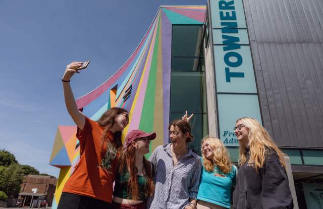 A group of young people take their photo in front of the colourful exterior of Towner gallery, Eastbourne
