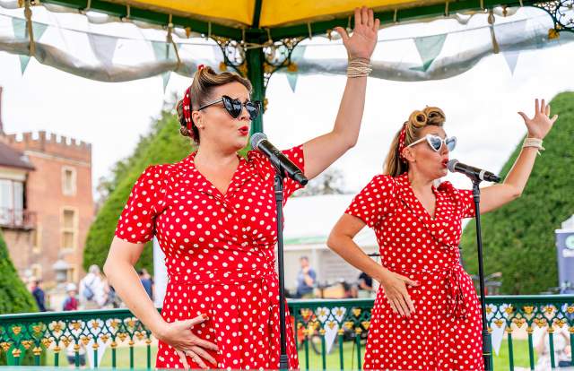 Two ladies wearing red polka dot dresses sing on a bandstand in Sussex