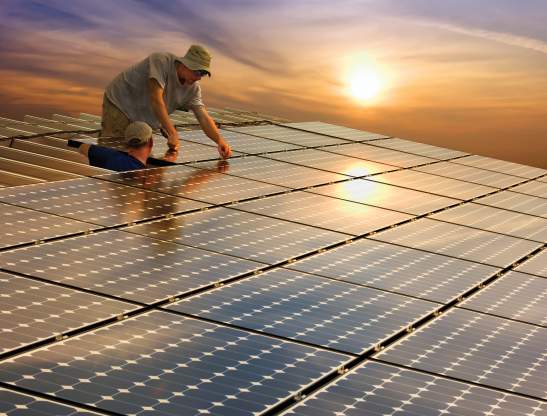 two construction workers installing solar panels on the roof of a house