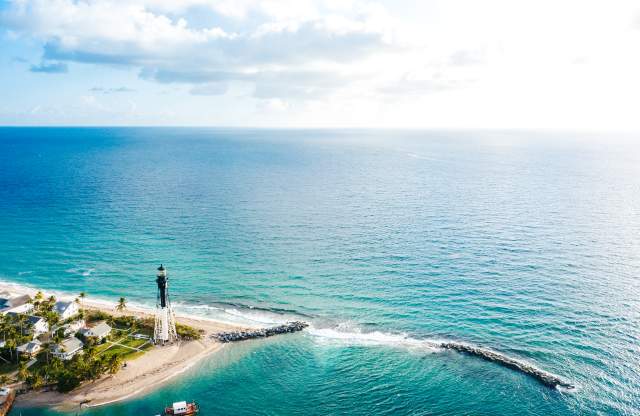 The Hillsboro Lighthouse stands at the edge of the Hillsboro Inlet, surrounded by the crystal blue Florida coastline