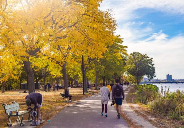 People sitting on benches and others walking on paved path along the Charles River Esplanade of Boston