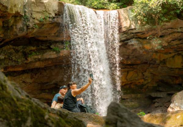 A family takes a selfie in front of a waterfall.