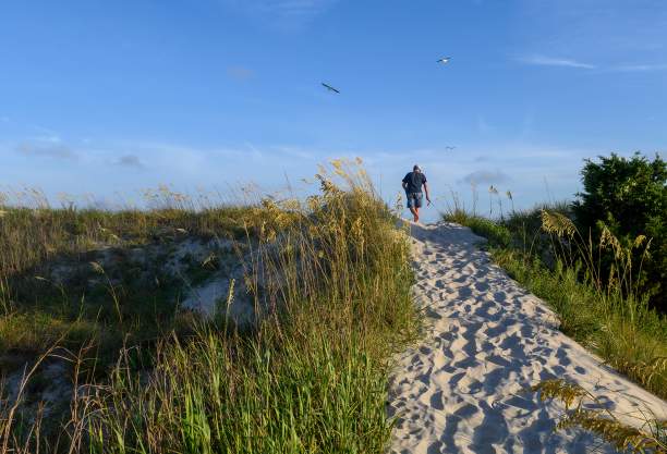 a man walking on a sandy beach path over the dunes on Oak Island, NC