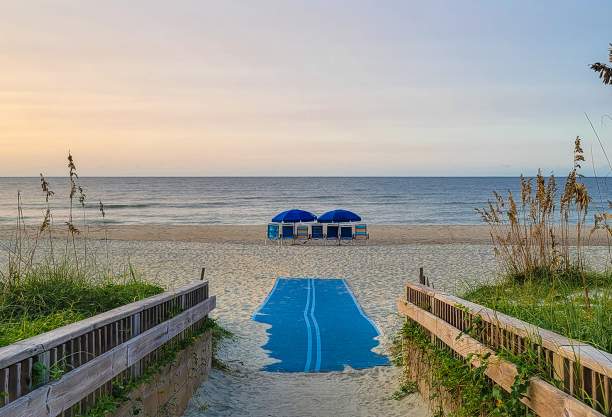 a wooden walkway and ADA beach mat leading out onto a beach with chairs and umbrellas in view