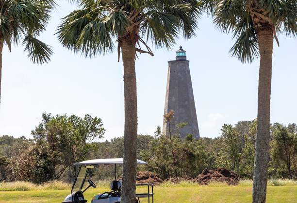 a gold cart parked on a road between palm trees with a triangular stone lighthouse in the background