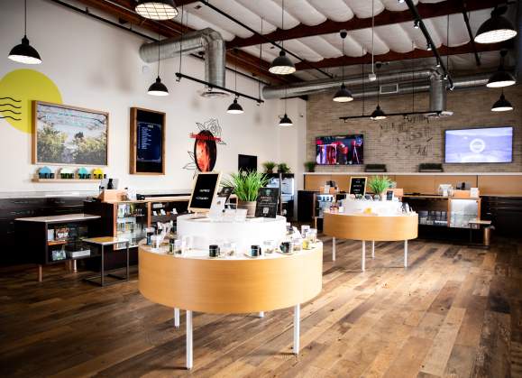 Interior of a Farmacy cannabis shop with modern wooden displays, product cases, bright lighting, art walls, and an open retail layout.
