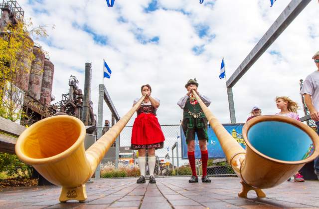A man and woman in traditional German attire playing large trumpets on a stage