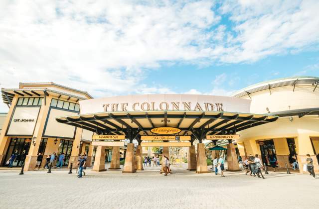 Entrance to The Colonnade at Sawgrass shopping mall with people walking and stores on a sunny day under a partly cloudy sky.