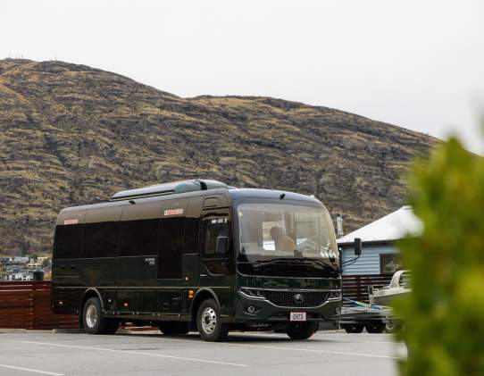 A green electric bus parked outside the Queenstown marina with a mountain in the background