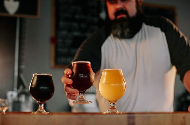 A bartender sets down a glass of beer in a beer flight featuring a dark beer, amber beer, and wheat beer.