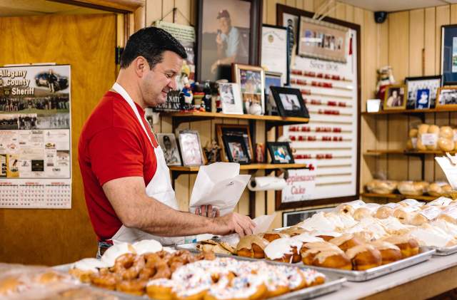 A man in a red shirt grabs a donut to put in a bag for a customer.