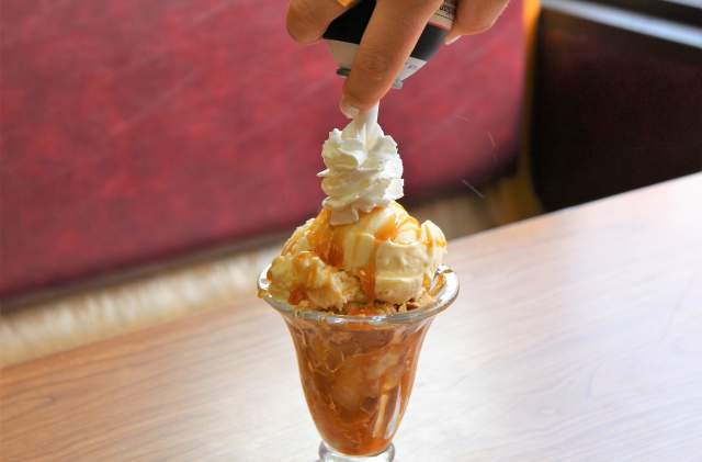 Someone adds whipped cream topping to the top of an apple pie sundae creation.