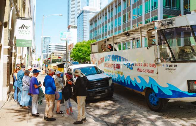 People line up on the sidewalk outside of the Austin Visitor Center waiting to board the Duck Tour vehicle