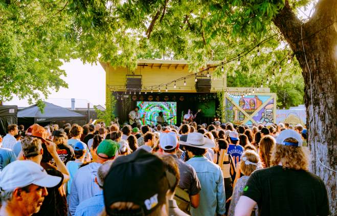 Image of a band performing on a small yellow framed stage with a large group of people standing in front of the stage.