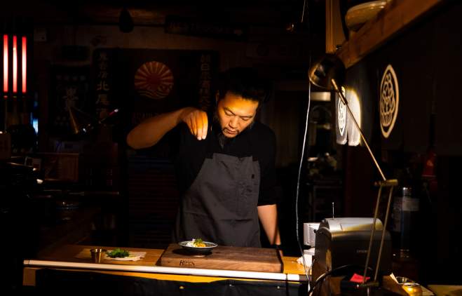 Chef Tatsu Aikawa sprinkles ingredients over a dish