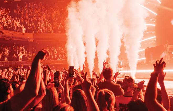 Photo from the audience looking up at the stage at ACL Live music venue. There are smoke machines at the front, and the room is tinged in red/orange light