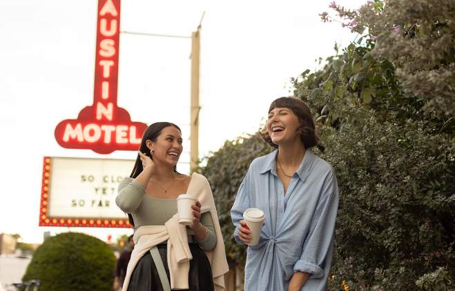 Two women walking and laughing on South Congress Avenue. Austin Motel neon sign is lit up in background