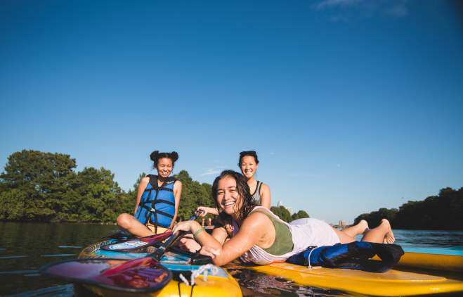 Photo of three women sitting on Lady Bird Lake paddle board rentals from Rowing Dock. They are looking and smiling at the camera, which sits at water-level